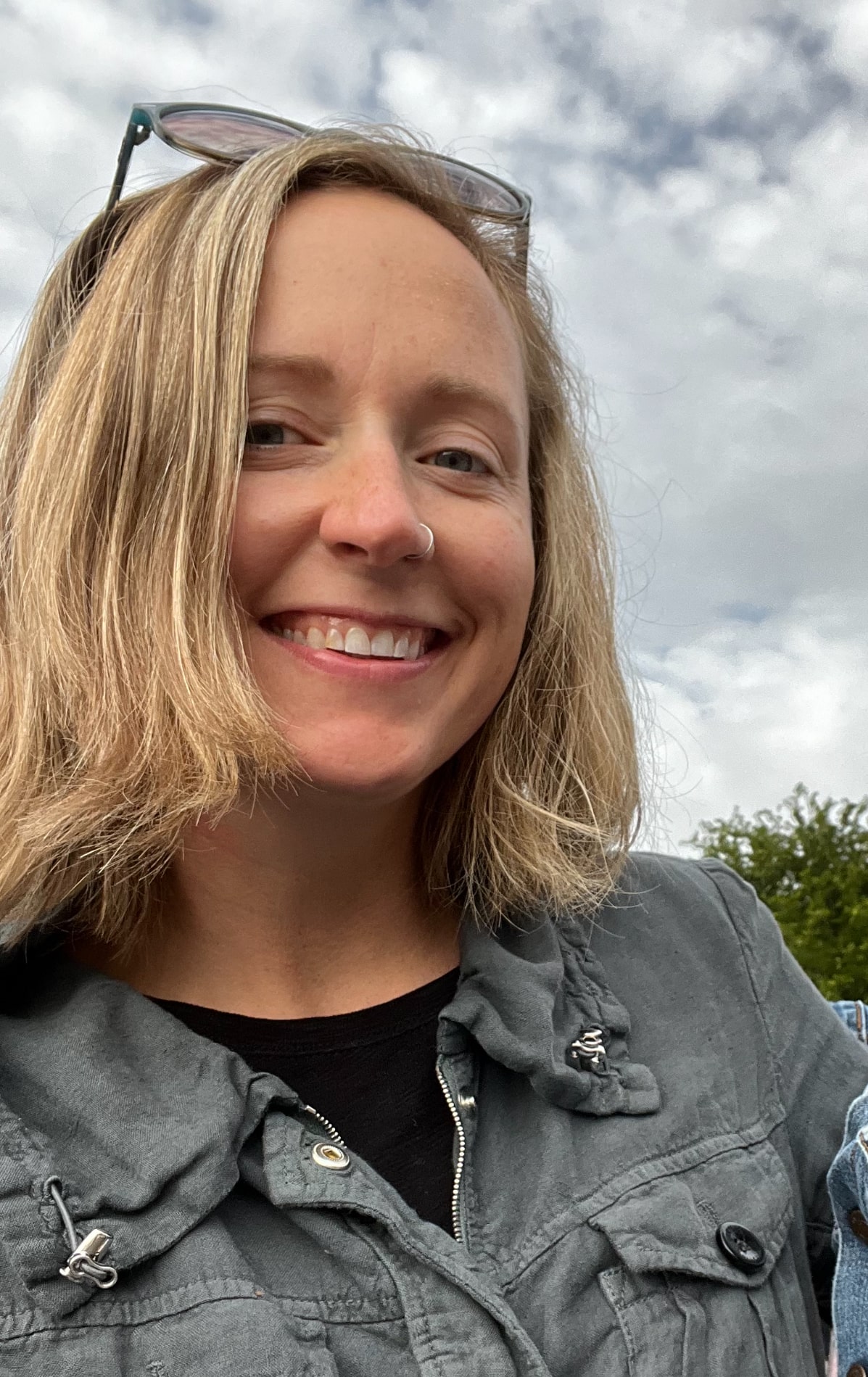 A smiling woman with blonde hair and sunglasses poses for the camera, exuding confidence and joy