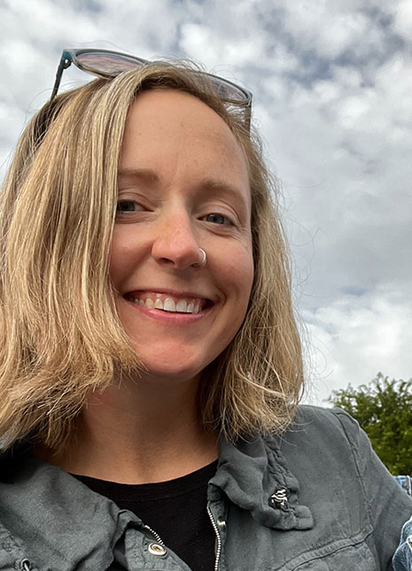 A smiling woman with blonde hair and sunglasses poses for the camera, exuding confidence and joy