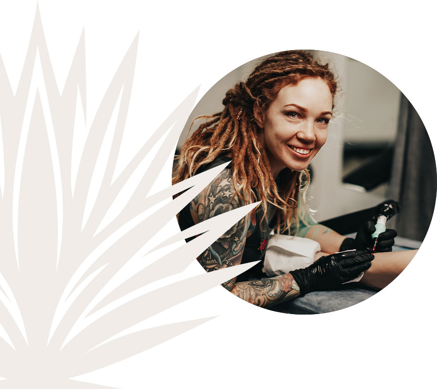 A woman with dreadlocks sits on a chair, showcasing her tattoo, exuding confidence and individuality.