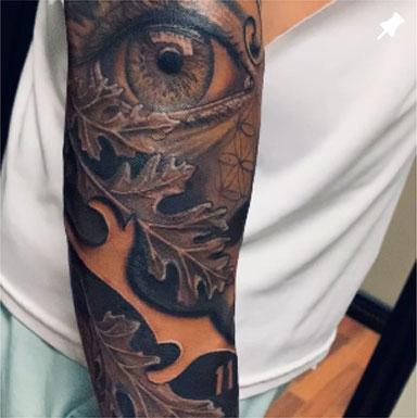 A detailed view of a man's arm displaying a tattoo of an eye entwined with delicate leaves, highlighting artistic expression.